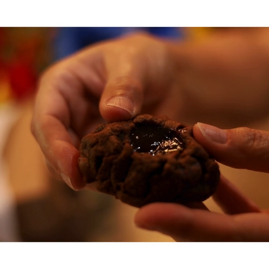 Hand Grabbing Lava Cookie and breaking it open, showing the texture of the raspberry lava and triple-chocolate cookie